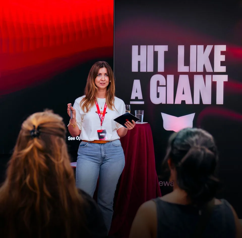 A speaker on stage in front of a screen reading “Hit like a giant”.